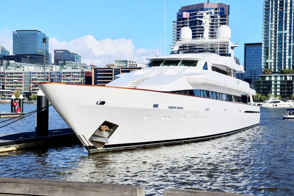 Sleek white luxury yacht docked in a modern urban marina with skyscrapers in the background.